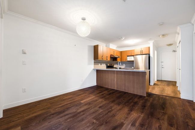 Kitchen featuring white microwave, a peninsula, under cabinet range hood, dark wood-style flooring, and light countertops | Image 7