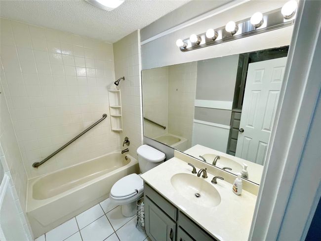 Full bath featuring a textured ceiling, toilet, shower / bath combination, tile patterned flooring, and vanity | Image 9