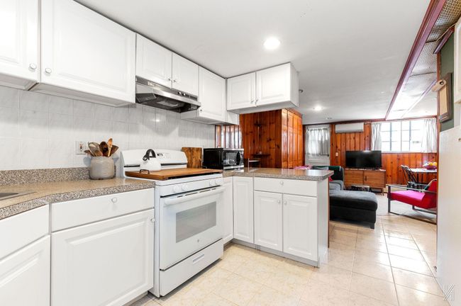 Kitchen with white range oven, under cabinet range hood, black microwave, wooden walls, and a wall mounted AC | Image 14