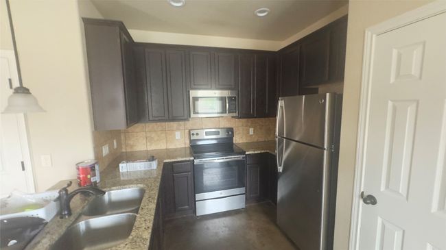 Kitchen with appliances with stainless steel finishes, tasteful backsplash, light stone countertops, and concrete floors | Image 5