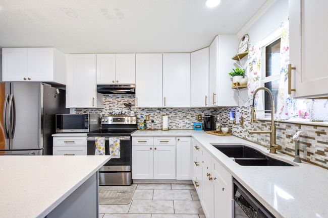 Kitchen with under cabinet range hood, stainless steel appliances, tasteful backsplash, and light stone countertops | Image 8