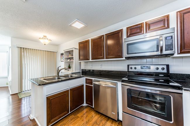 Kitchen with dark wood finished floors, dark countertops, appliances with stainless steel finishes, and a sink | Image 4