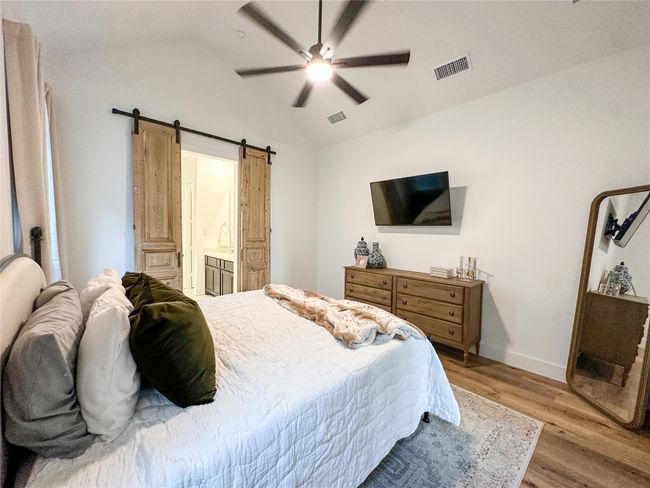 Bedroom with wood finished floors, a barn door, vaulted ceiling, ceiling fan, and ensuite bath | Image 19