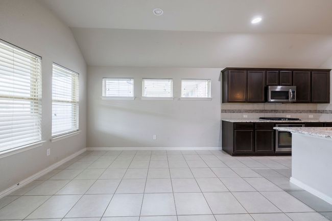 Kitchen with appliances with stainless steel finishes, lofted ceiling, decorative backsplash, dark brown cabinetry, and light tile patterned floors | Image 17