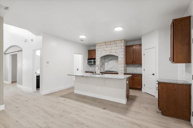 Kitchen with backsplash, light wood-style floors, a kitchen island with sink, arched walkways, and light stone countertops | Image 8