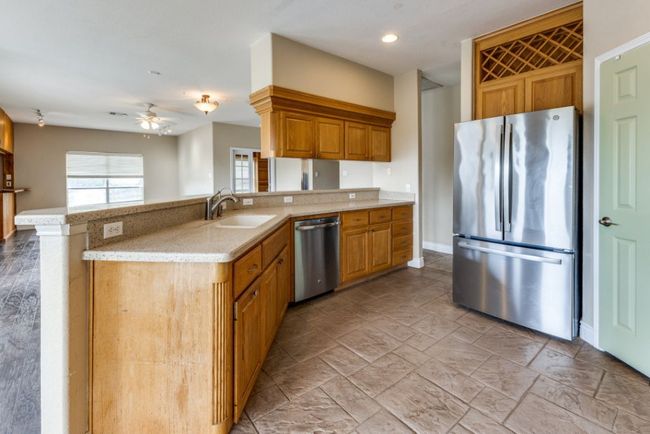 Kitchen with brown cabinets, light stone counters, stainless steel appliances, a sink, and ceiling fan | Image 10