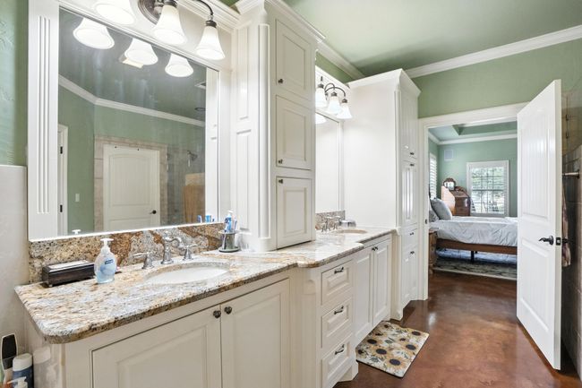 Ensuite bathroom featuring crown molding, double vanity, finished concrete floors, and tiled shower | Image 18