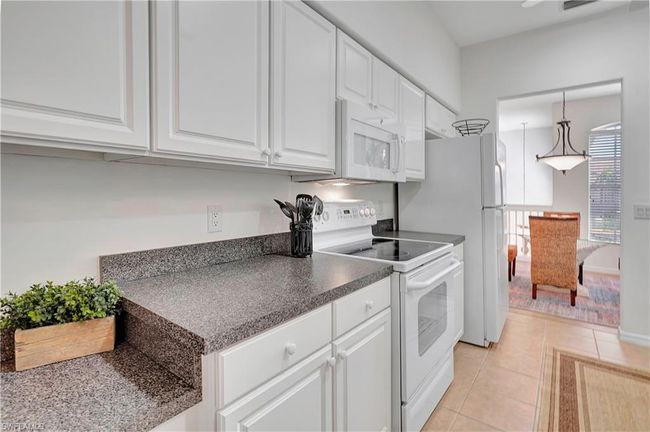 Kitchen featuring white cabinetry, white appliances, light tile patterned floors, pendant lighting, and ceiling fan | Image 13