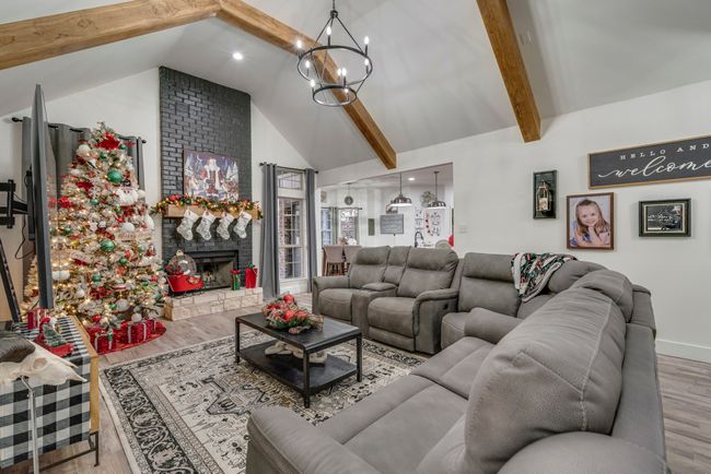 Living room with vaulted ceiling with beams, light hardwood / wood-style floors, a stone fireplace, and an inviting chandelier | Image 5