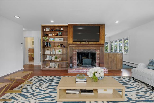 Living room with wood-burning fireplace, built-in shelving, hardwood flooring. Virtually staged. | Image 4
