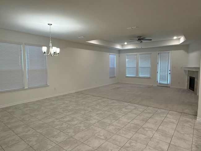 Unfurnished living room featuring a tray ceiling, a ceiling fan, a chandelier, a tiled fireplace, and light colored carpet | Image 19