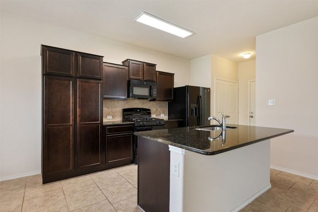Kitchen with black appliances, a sink, decorative backsplash, a center island with sink, and baseboards | Image 16