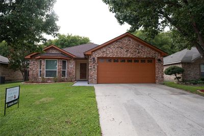 Ranch-style home featuring central air condition unit, a front yard, and a garage | Image 1