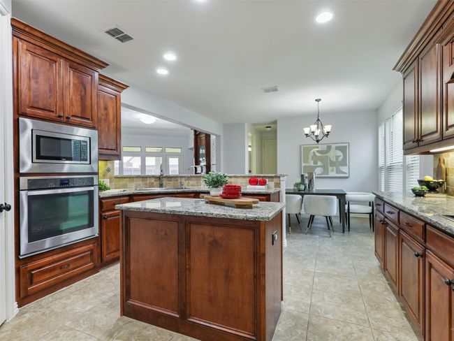 Kitchen featuring stainless steel appliances, tasteful backsplash, a kitchen island, a chandelier, and light stone countertops | Image 8