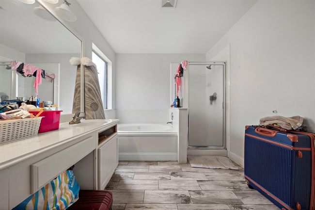 The primary bath offers a spa-inspired layout with a deep soaking tub beneath a frosted privacy window and a separate walk-in shower enclosed in glass. Dual vanities provide ample counter space and storage, making morning routines efficient for two. Wood-look tile floors bring warmth and durability to the space. | Image 17