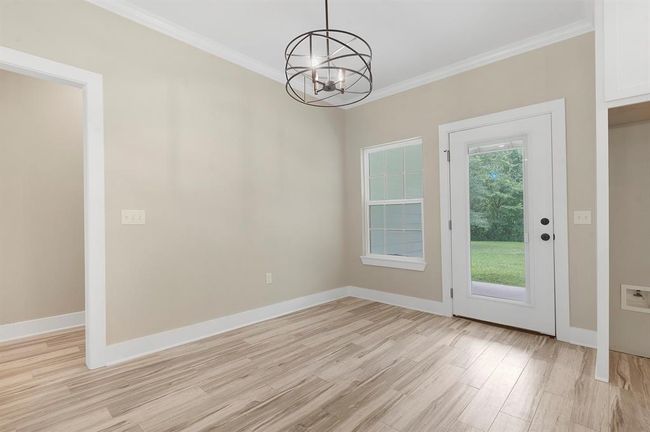 This is a bright, neutral-colored room featuring wood-style flooring and a modern light fixture. It has a window and a glass door leading to a grassy backyard, offering natural light and easy outdoor access. | Image 8