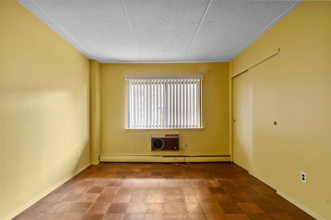 Unfurnished bedroom featuring a textured ceiling, an AC wall unit, a baseboard radiator, and a closet | Image 21
