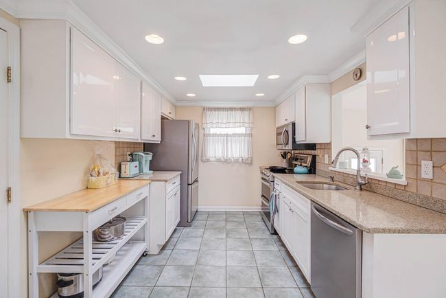 Kitchen featuring a sink, baseboards, white cabinetry, a skylight, and appliances with stainless steel finishes | Image 20