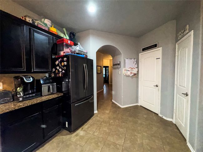 Kitchen featuring light tile patterned floors, baseboards, arched walkways, freestanding refrigerator, and dark cabinetry | Image 8