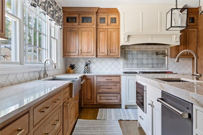 Kitchen with stainless steel appliances, a sink, glass insert cabinets, light stone countertops, and brown cabinetry | Image 19