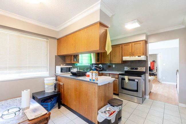 Kitchen featuring stainless steel range with electric stovetop, under cabinet range hood, white microwave, decorative backsplash, and a peninsula | Image 6