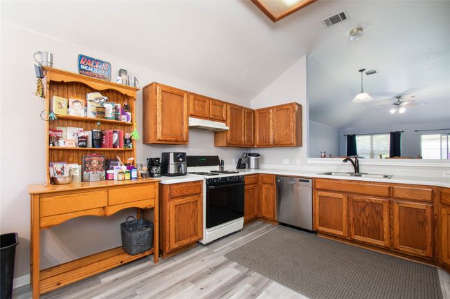 Kitchen featuring range with gas stovetop, under cabinet range hood, visible vents, dishwasher, and a sink | Image 7