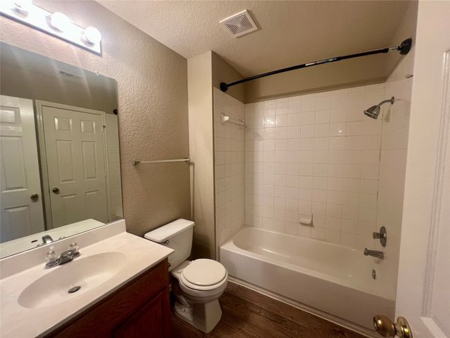 Full bathroom with a textured wall, wood finished floors, vanity, a textured ceiling, and shower combination | Image 34