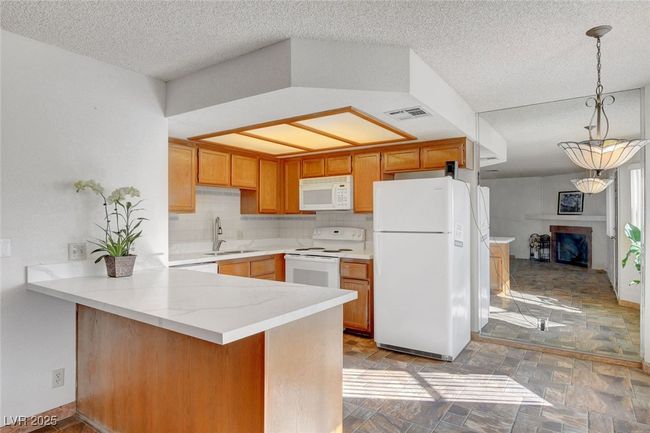 Kitchen with white appliances, a peninsula, a textured ceiling, visible vents, and a sink | Image 8