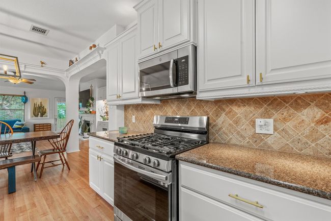 Kitchen with stainless steel appliances, light wood finished floors, white cabinetry, decorative backsplash, and ceiling fan | Image 10