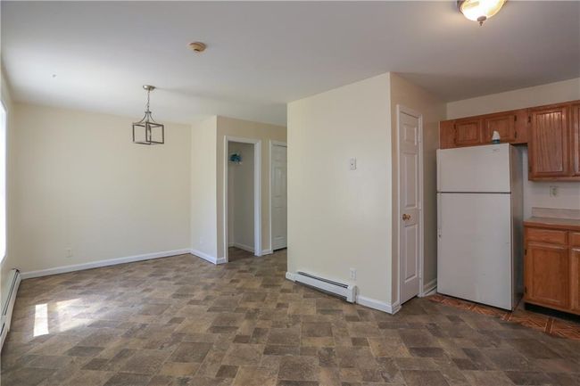 Kitchen featuring freestanding refrigerator, a baseboard heating unit, stone finish flooring, baseboards, and brown cabinets | Image 5