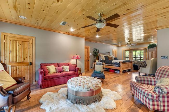 This spacious room features warm wood paneling on the ceiling and hardwood floors, creating a cozy, rustic atmosphere. It includes a sitting area with comfortable furniture, a large bed, and ample natural light from multiple windows. The neutral walls and wooden doors add to the inviting, homey vibe. | Image 30