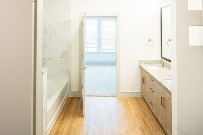 Full bathroom featuring a washtub, a sink, wood finished floors, baseboards, and double vanity | Image 6