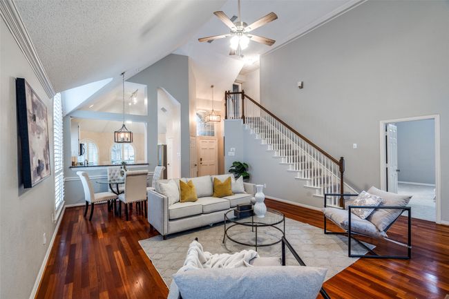Living area featuring stairs, wood finished floors, a ceiling fan, high vaulted ceiling, and baseboards | Image 5