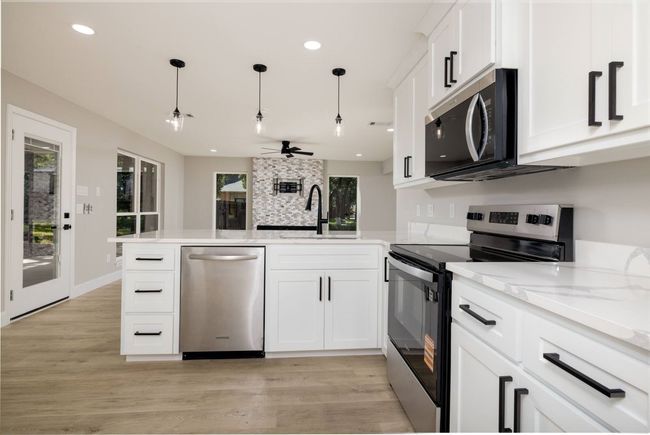 Kitchen featuring stainless steel appliances, a peninsula, white cabinetry, light wood-type flooring, and pendant lighting | Image 20