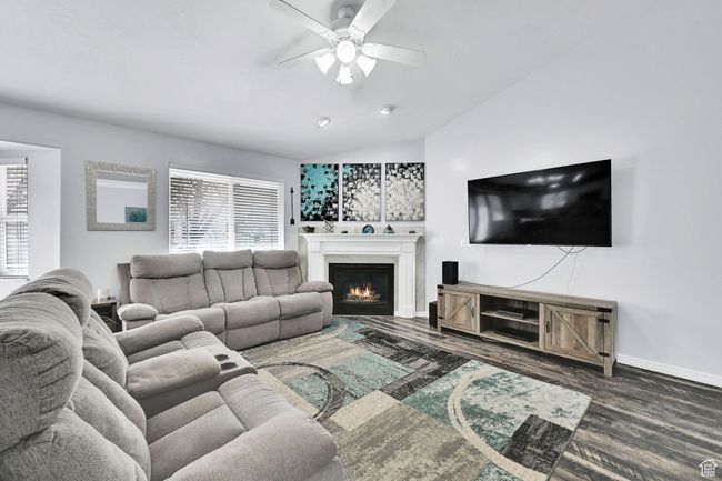 Living room featuring vaulted ceiling, a lit fireplace, ceiling fan, and a healthy amount of sunlight | Image 9