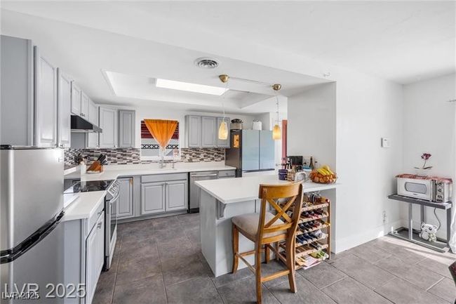 Kitchen with appliances with stainless steel finishes, under cabinet range hood, a raised ceiling, gray cabinets, and backsplash | Image 14