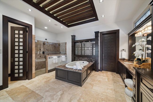 This tranquil primary bathroom includes an expansive glass-enclosed walk-in shower with multiple shower heads and built-in bench seating. A separate lavatory, tucked behind an 8-foot wood and opaque glass door, offers added privacy. Thoughtfully designed by famed Miami based designer, Adriana Hoyos, this ensuite retreat blends sophisticated style with resort-inspired comfort, creating a spa-like experience perfect for relaxation and daily indulgence. | Image 28