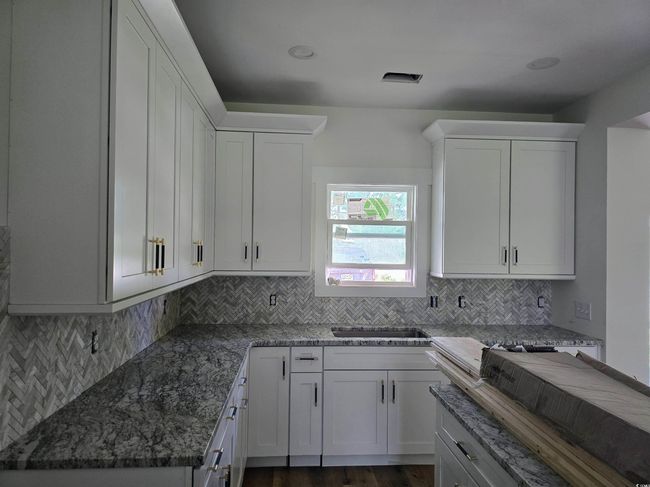 Kitchen with dark stone counters, white cabinets, tasteful backsplash, and a sink | Image 12