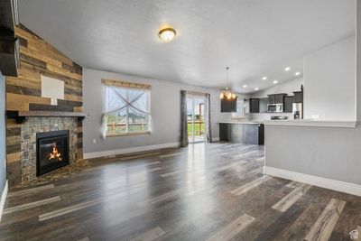 Unfurnished living room featuring an inviting chandelier, a textured ceiling, lofted ceiling, wood walls, and dark wood-type flooring | Image 3