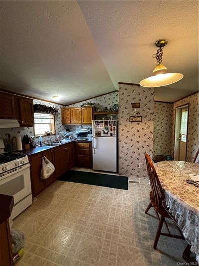 Kitchen featuring range, stainless steel refrigerator, a textured ceiling, lofted ceiling, and tile patterned floors | Image 3