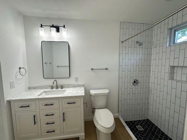 Bathroom with tiled shower, toilet, vanity, wood finished floors, and baseboards | Image 22