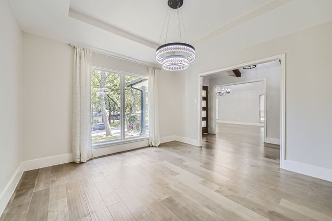 Unfurnished dining area featuring a tray ceiling, an inviting chandelier, baseboards, and light wood-style floors | Image 7