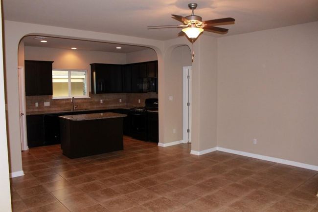 Kitchen with black appliances, arched walkways, dark cabinetry, decorative backsplash, and a kitchen island | Image 5