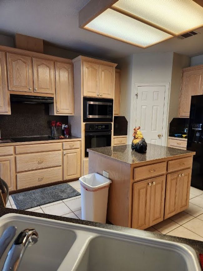 Kitchen featuring black appliances, light tile patterned floors, light brown cabinets, and a center island | Image 25