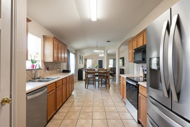 Kitchen featuring stainless steel appliances, light countertops, vaulted ceiling, tasteful backsplash, and light tile patterned floors | Image 5