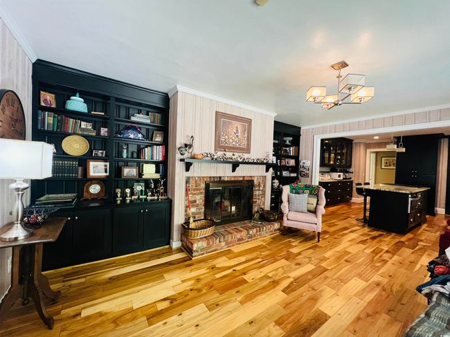 Living area featuring crown molding, a fireplace, wood finished floors, and a chandelier | Image 7