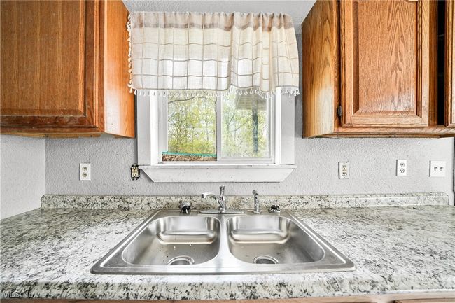 Kitchen featuring a textured wall, a sink, and brown cabinetry | Image 4
