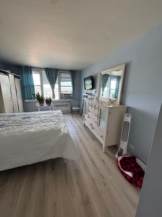 Bedroom with multiple windows, light wood-style flooring, radiator, and cooling unit | Image 5