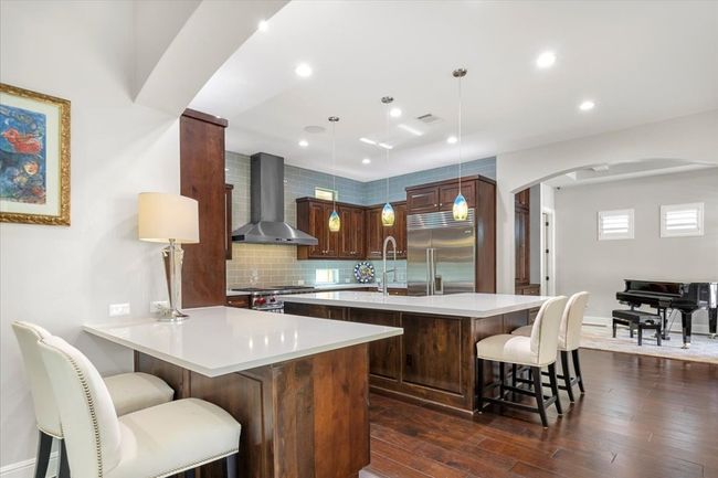 Kitchen featuring a kitchen breakfast bar, premium appliances, arched walkways, wall chimney exhaust hood, and visible vents | Image 10