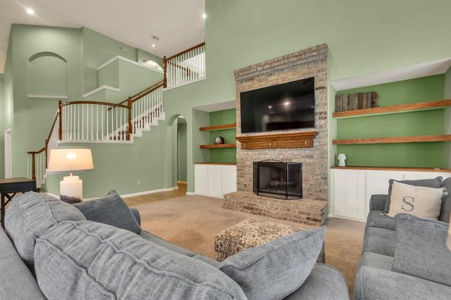 Living room featuring carpet flooring, baseboards, a high ceiling, stairs, and a fireplace | Image 16